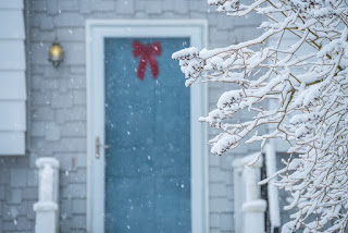 A cozy door and porch of a small house during a snowfall. Branches of plants covered with fluffy snow. USA. Maine. The atmosphere of a beautiful white winter and home comfort